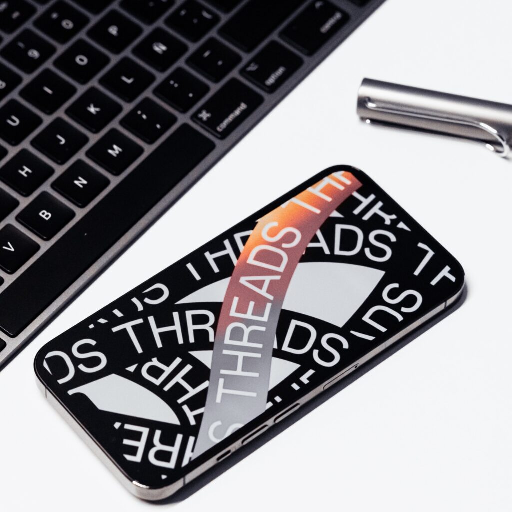 Overhead photo of a mobile phone with a Threads app graphic next to a keyboard and pen