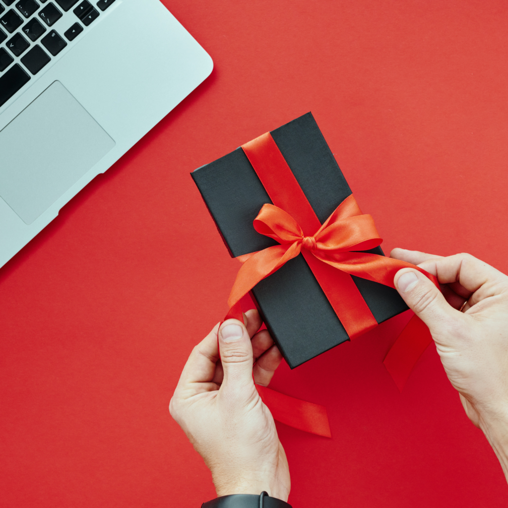 Overhead image of man wrapping a present next to his laptop to indicate adding value to an offer
